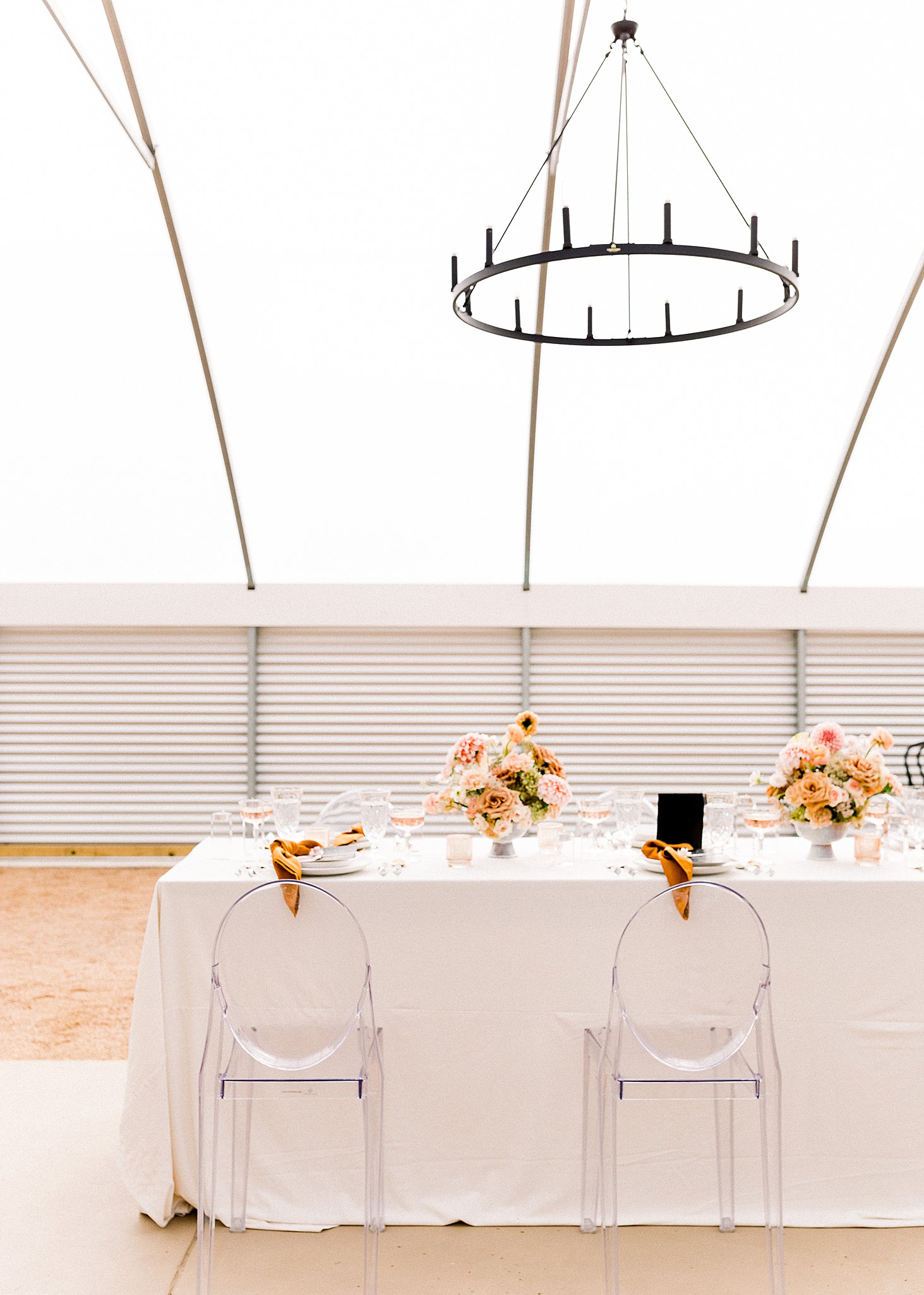 Wedding reception table with clear chairs and peach bouquets
